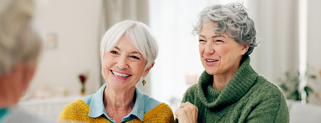 Image of two senior women sitting across from a senior man and laughing with him